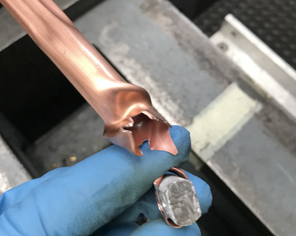 A piece of twisted copper tube that has sheared during the forming process