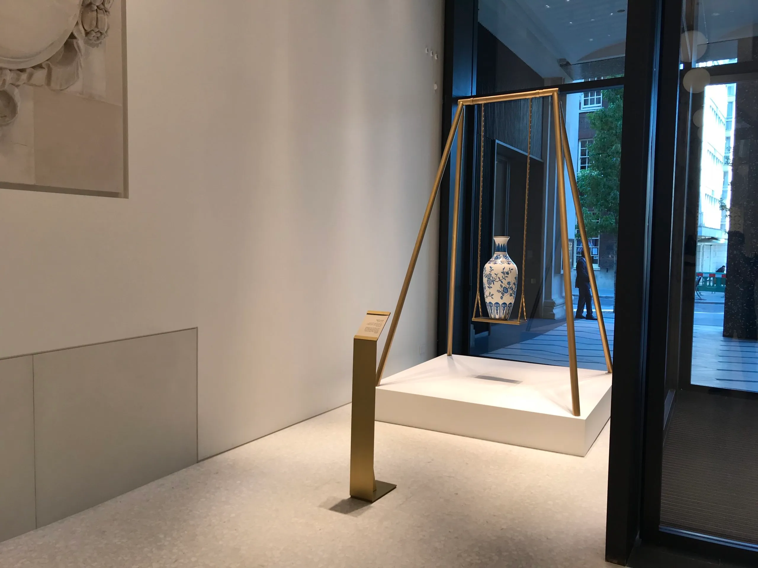 Ornate vase being displayed on a luxury swing style platform supported by lengths of brass twisted square tubing in a satin finish